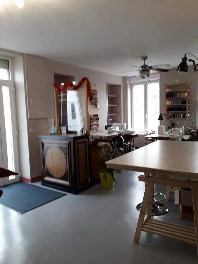 L'atelier : table de coupe sur tréteaux, machines à coudre, étagère de bobines de fil et grand miroir