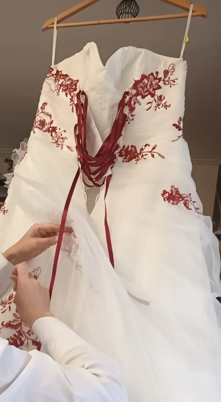 Robe de mariée blanche brodée de rouge, sur un cintre, tenue à deux mains